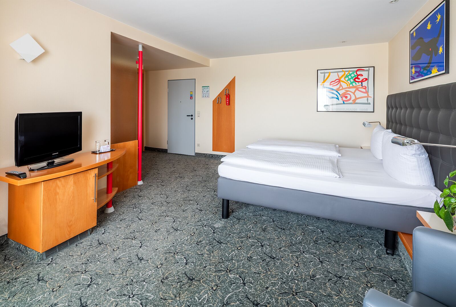 Quarto de hotel com cama, televisão, escrivaninha e porta que dá para outro aposento.