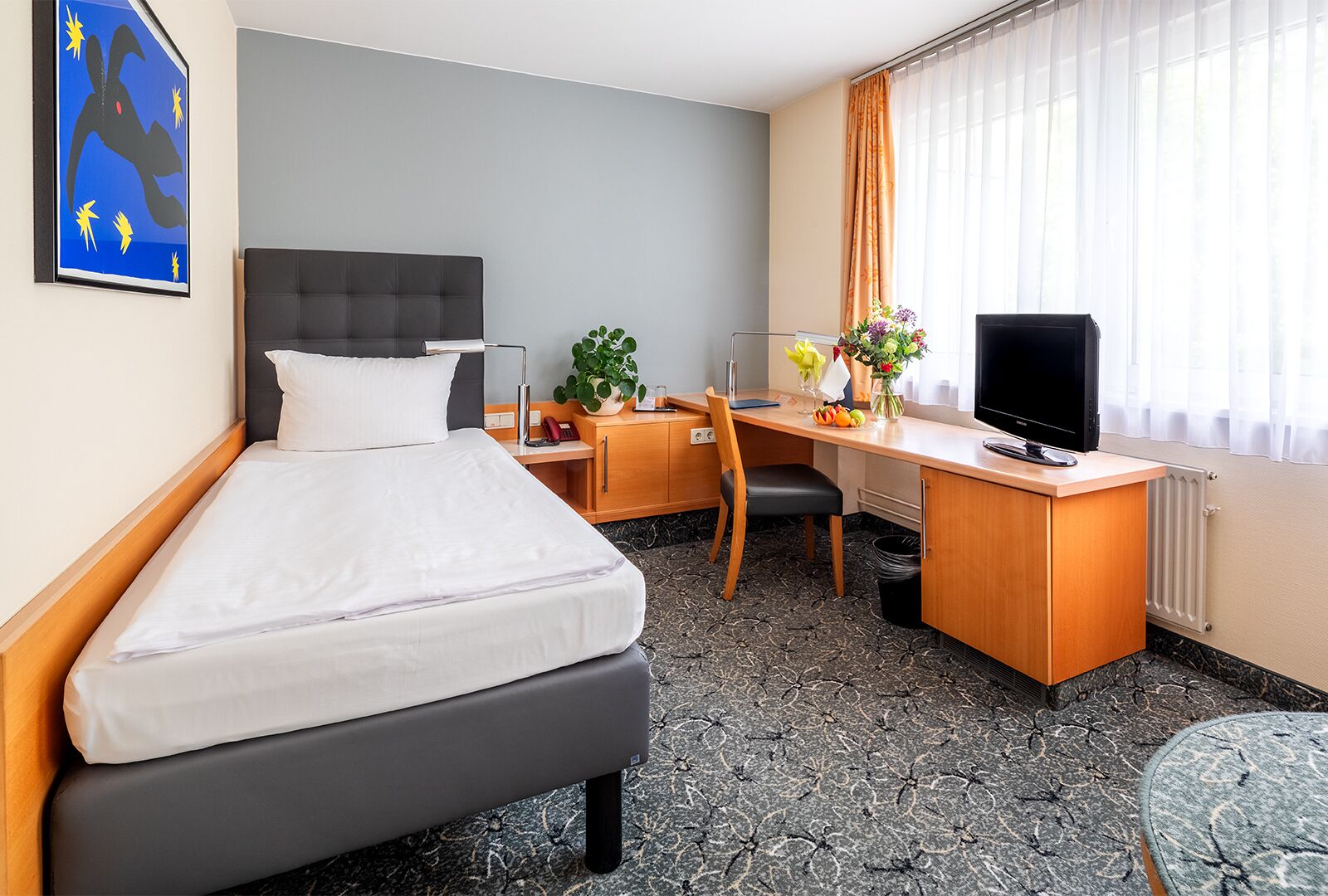 Une chambre d’hôtel équipée d’un lit, d’un bureau, d’une chaise, d’une télévision et d’une fenêtre avec des rideaux.