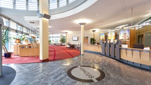 A spacious lobby with a red carpet, a reception desk, and a large circular logo on the floor. - Abacus Tierpark Hotel Berlin (Berlin)