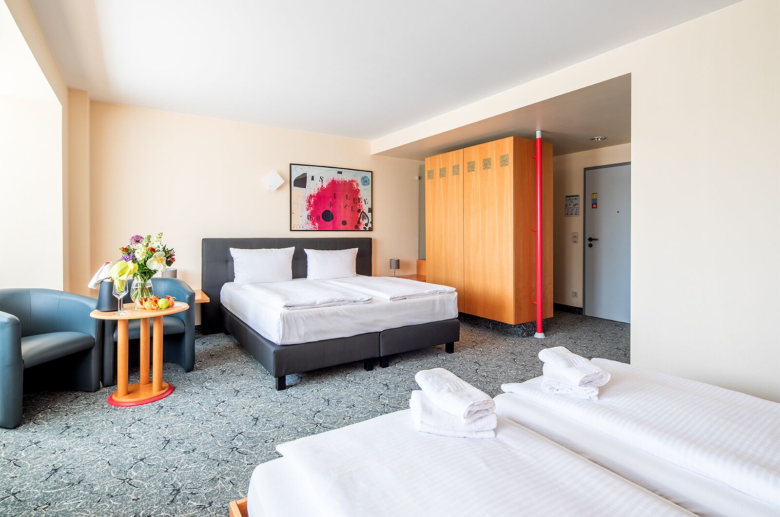 Una habitación de hotel con una cama, un escritorio con un florero, una silla y un armario.