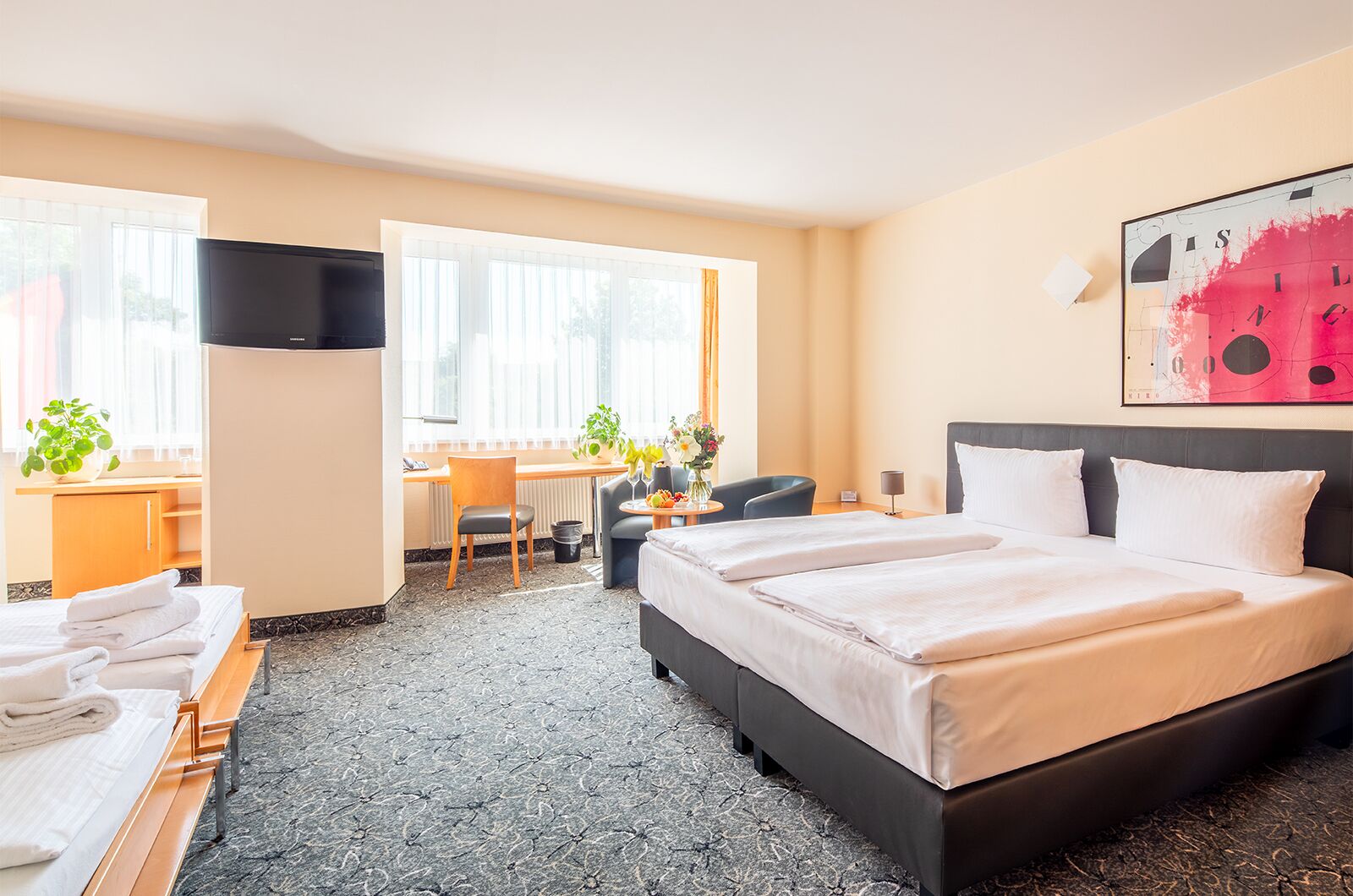 Habitación de hotel con cama, escritorio, silla, televisor y ventana.