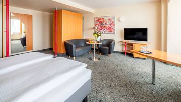 A hotel room with a bed, a desk, a TV, a sofa, and a chair.