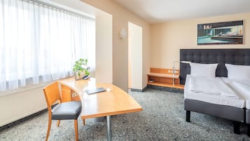 Habitación de hotel con cama, escritorio, una silla, una planta y un cuadro en la pared.