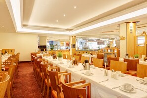 A hotel dining area with multiple tables set for breakfast, wooden chairs, and a buffet counter in the background. - Abacus Tierpark Hotel Berlin (Berlin)
