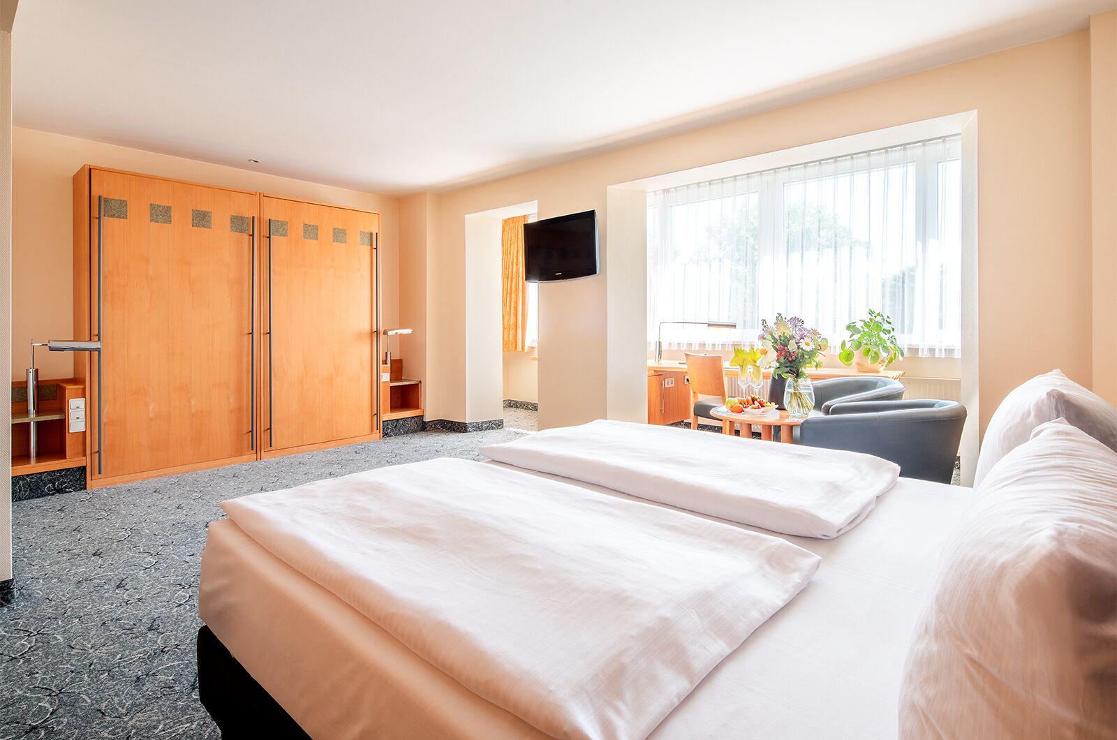 A hotel room with a bed, a desk, a chair, a TV, and a window with curtains.