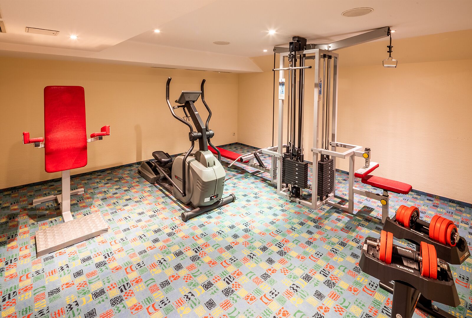 Un gimnasio con equipo de ejercicio, un banco rojo y un suelo estampado.