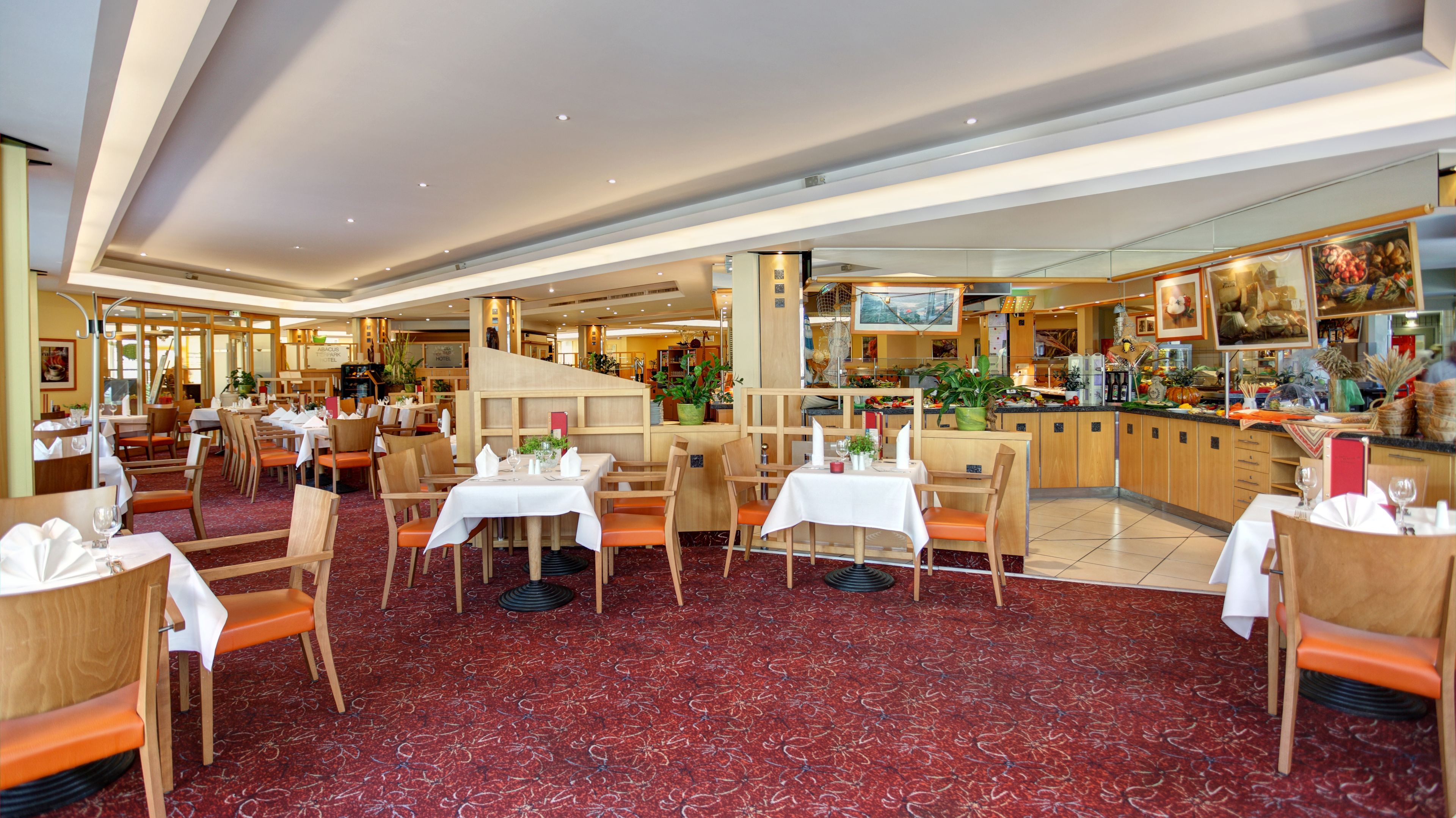 En rymlig hotellrestaurang med flera matplatser, en central bar och utsikt över köket.