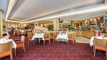 En rymlig hotellrestaurang med flera matplatser, en central bar och utsikt över köket.