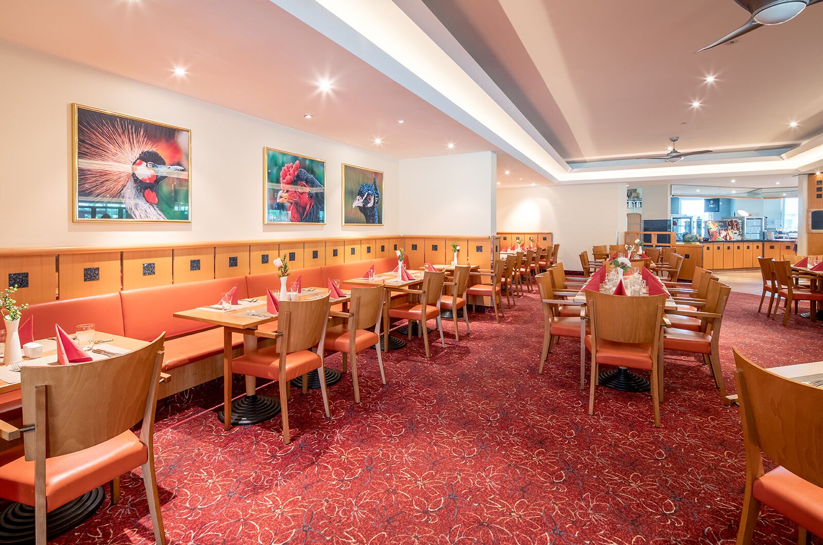 A restaurant with wooden booths and tables, red carpet flooring, and wall-mounted artwork.
