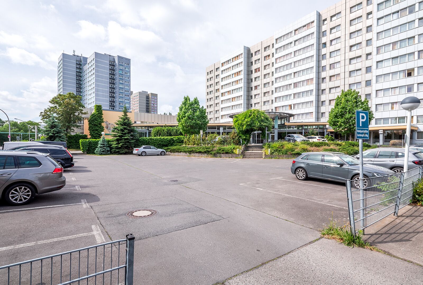 Un parking rempli de voitures, un bâtiment à l’architecture moderne et un ciel dégagé.