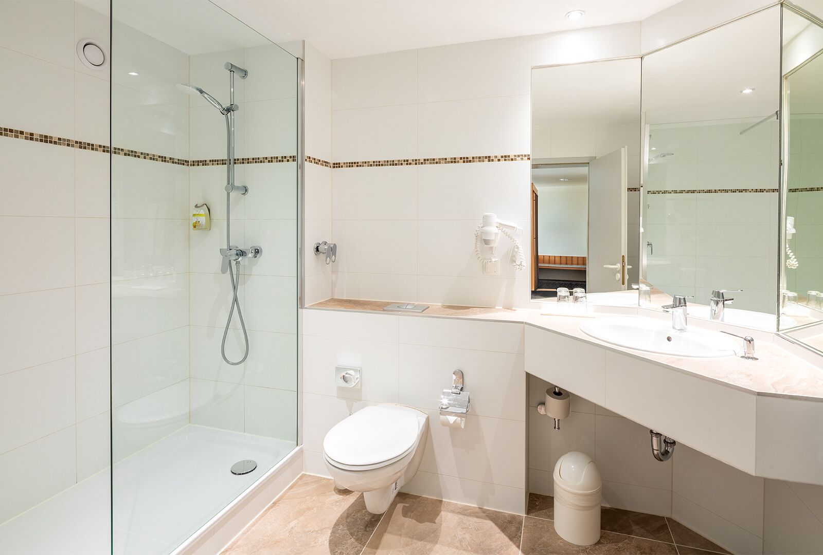 Un baño moderno con ducha de vidrio, inodoro, lavamanos con espejo y un cubo de basura.