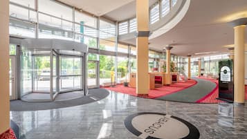 Un vestíbulo de hotel con puerta giratoria, mostrador de recepción y área alfombrada en rojo.