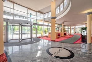 Un vestíbulo de hotel con puerta giratoria, mostrador de recepción y área alfombrada en rojo.
