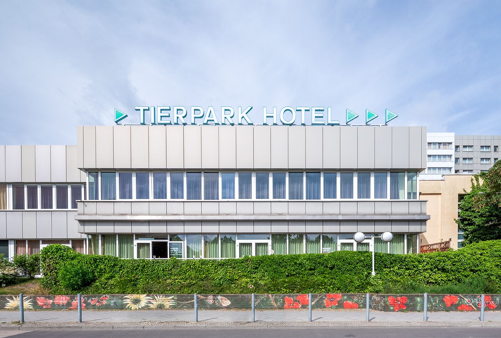 A modern hotel building with a sign reading 'TIERPARK HOTEL' and a clear sky above.