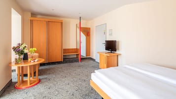 Ein Hotelzimmer mit einem Bett, einem Fernseher, einem Schreibtisch mit Blumenvase, einem Holzschrank und einer roten Stange.