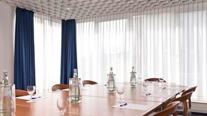 Uma sala de conferências com uma mesa comprida, cadeiras e garrafas de água.