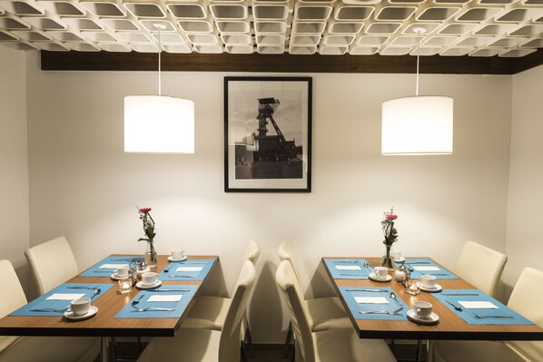 A dining area with two tables, each set with plates, cutlery, and napkins. There are two hanging pendant lights, and a framed picture on the wall. - Days Inn by Wyndham Dortmund West (Dortmund)