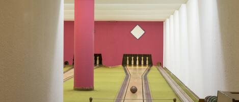 A bowling alley with green lanes, pink walls, and a white ceiling.