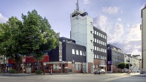 Hotel com uma torre imponente, placa de estacionamento e vista da rua com árvores e outros edifícios.