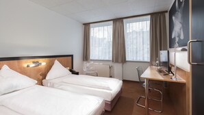 Quarto de hotel com duas camas, uma mesa, uma cadeira, uma televisão e uma janela com cortinas.