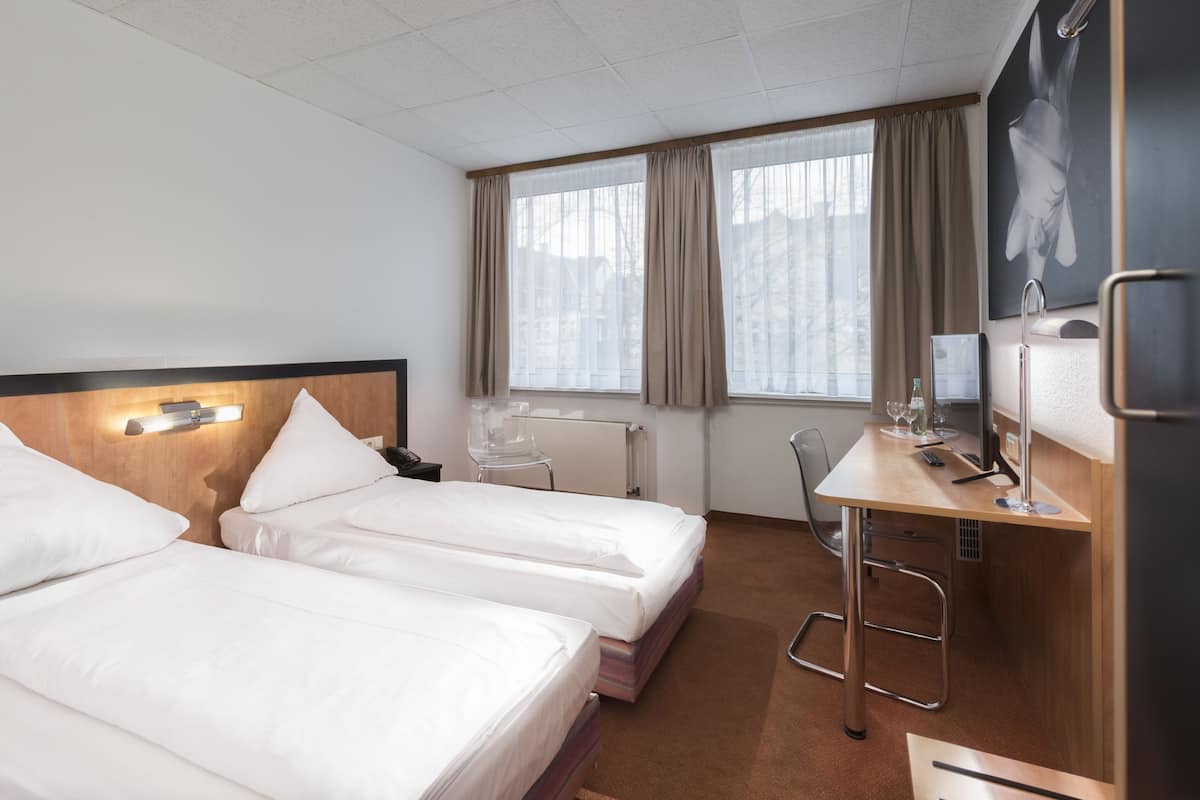 A hotel room with two beds, a desk, a chair, a TV, and a window with curtains.