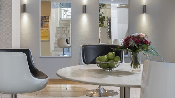 Uma sala de jantar moderna com uma mesa redonda, duas cadeiras, uma tigela de maçãs verdes e um vaso de flores.