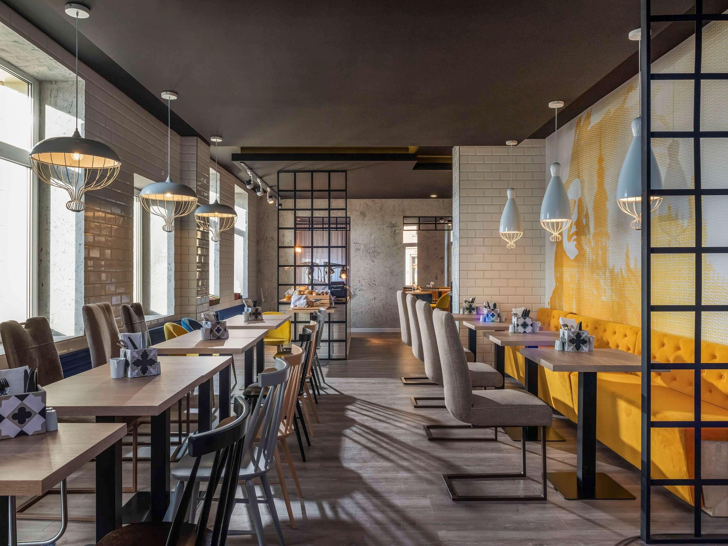 A modern restaurant interior with long communal tables, high ceilings, and pendant lighting.
