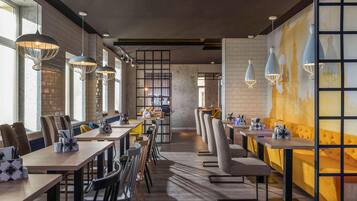 A modern restaurant interior with long communal tables, high ceilings, and pendant lighting.