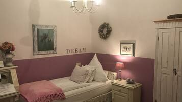 A bedroom with a bed, a nightstand, a dresser, a chandelier, and wall decorations including a painting and a wreath.
