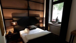 A bedroom with a large bed, two bedside tables, a window with a view, and a radiator. - Hotel Am Volksgarten (Düsseldorf)