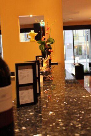 A reception area with a marble counter, a framed menu, and a decorative plant. - Concorde Hotel (Frankfurt)