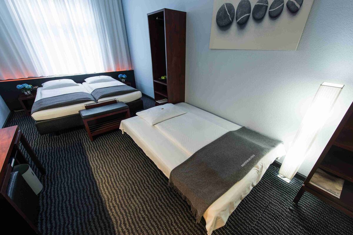 A hotel room with a large bed, a smaller bed, a desk, a wardrobe, and a wall with a stone artwork.