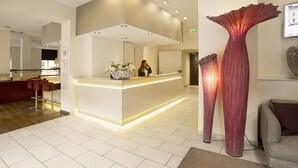 Un espace d’accueil moderne comprenant un comptoir central, un grand vase décoratif et un coin salon avec un canapé et des fauteuils.