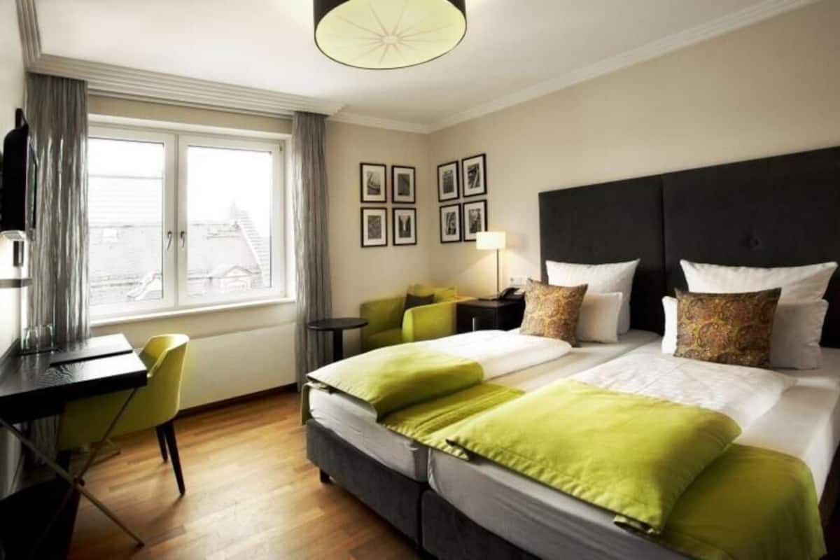A hotel room with two beds, a desk, a chair, and a window with curtains.