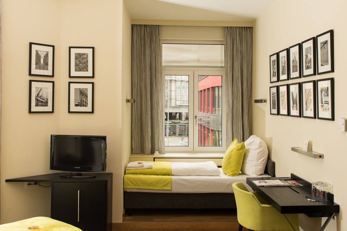 Quarto de hotel com duas camas, uma escrivaninha, televisão e janela com cortinas.