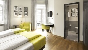 Une chambre d’hôtel avec un lit, un bureau, une chaise, une télévision et une salle de bain visible à travers une porte ouverte.
