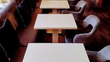A row of tables and chairs in a restaurant with a wooden floor and a large vase on a table in the background.