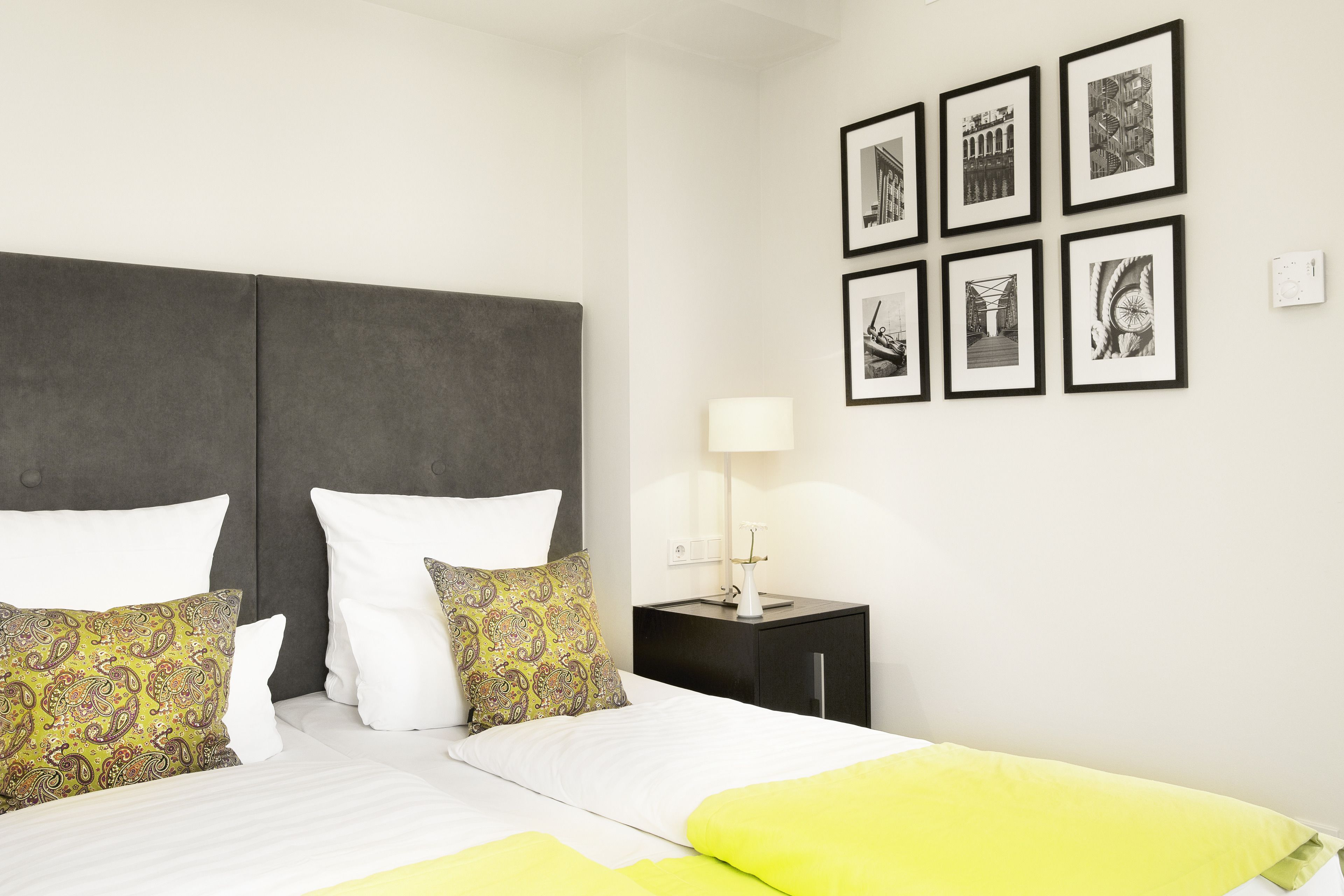 Quarto de hotel com uma cama, duas mesas de cabeceira e uma parede com quadros.