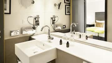 Une salle de bain moderne avec deux lavabos, un grand miroir et une vue sur une chambre à coucher comprenant un lit et une table de chevet.