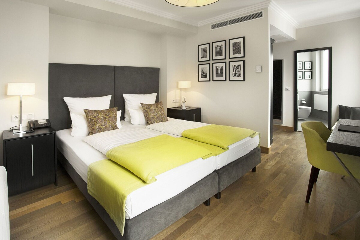 A modern hotel room with a large bed, bedside tables, a desk, and a mirror.