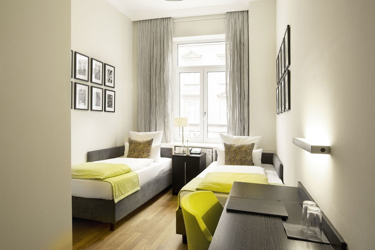 A hotel room with two beds, a desk, a chair, a lamp, and a window with curtains.