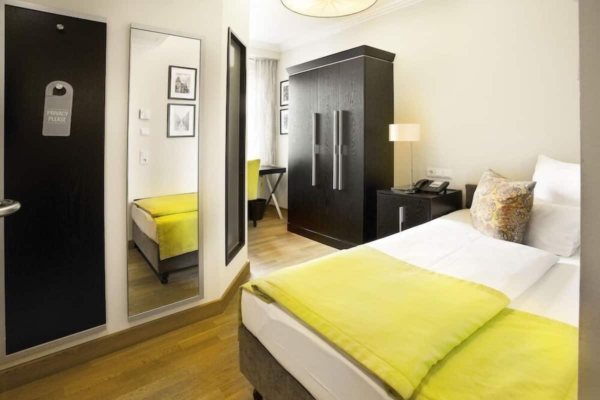 Ein Hotelzimmer mit einem Bett, einem Schrank, einem Schreibtisch mit Lampe und einem Spiegel.