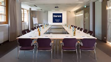 Ein Konferenzraum mit einem langen Tisch, violetten Stühlen und einem Bildschirm, der "Dorint Thermenhotel Freiburg" anzeigt.