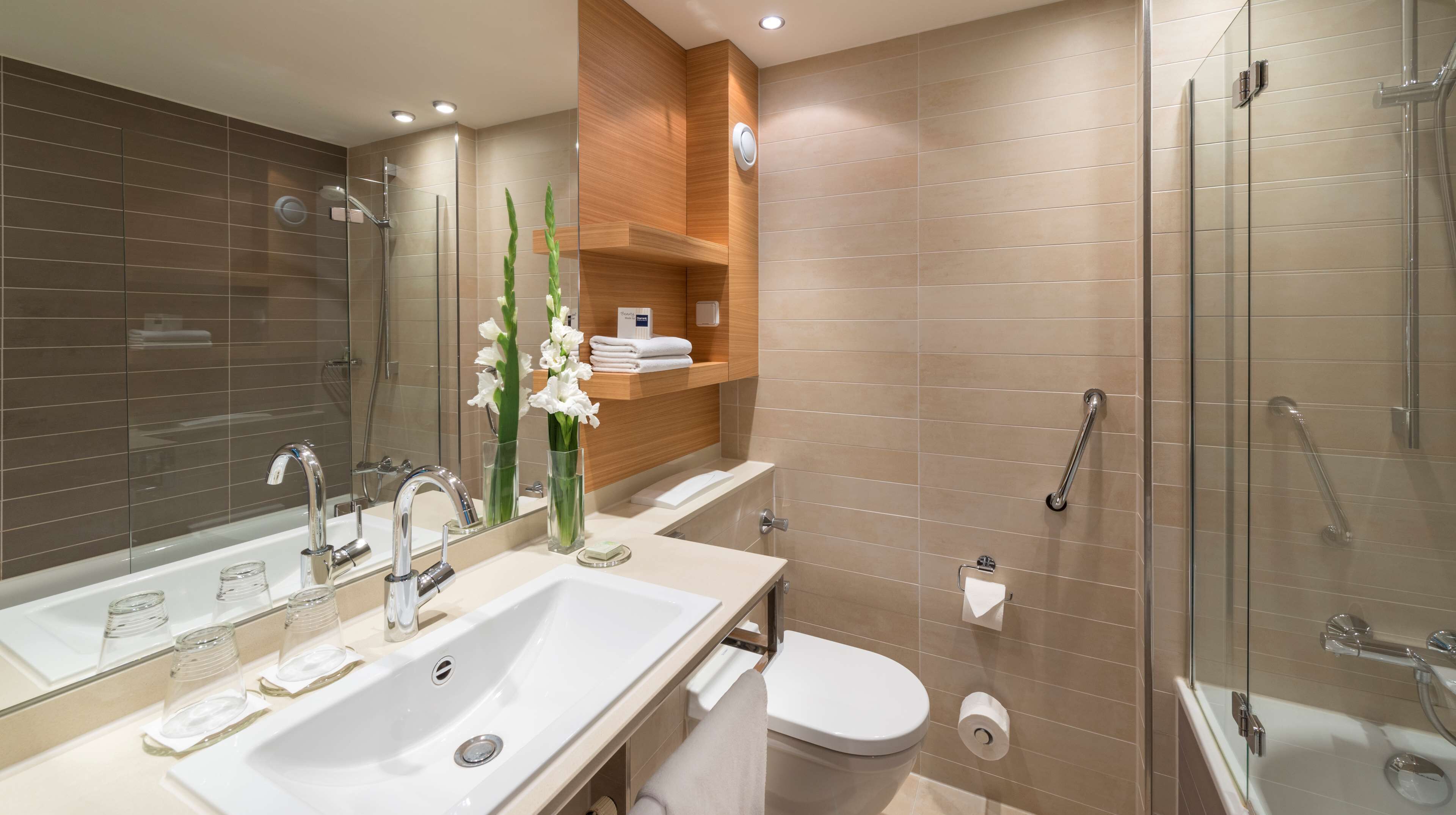 Ein modernes Badezimmer mit großem Spiegel, zwei Waschbecken, Toilette und einer Duschkabine.
