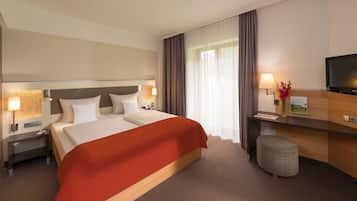 Habitación de hotel con una cama grande, un escritorio con televisor de pantalla plana, una mesita de noche con lámpara y una pequeña zona de estar.
