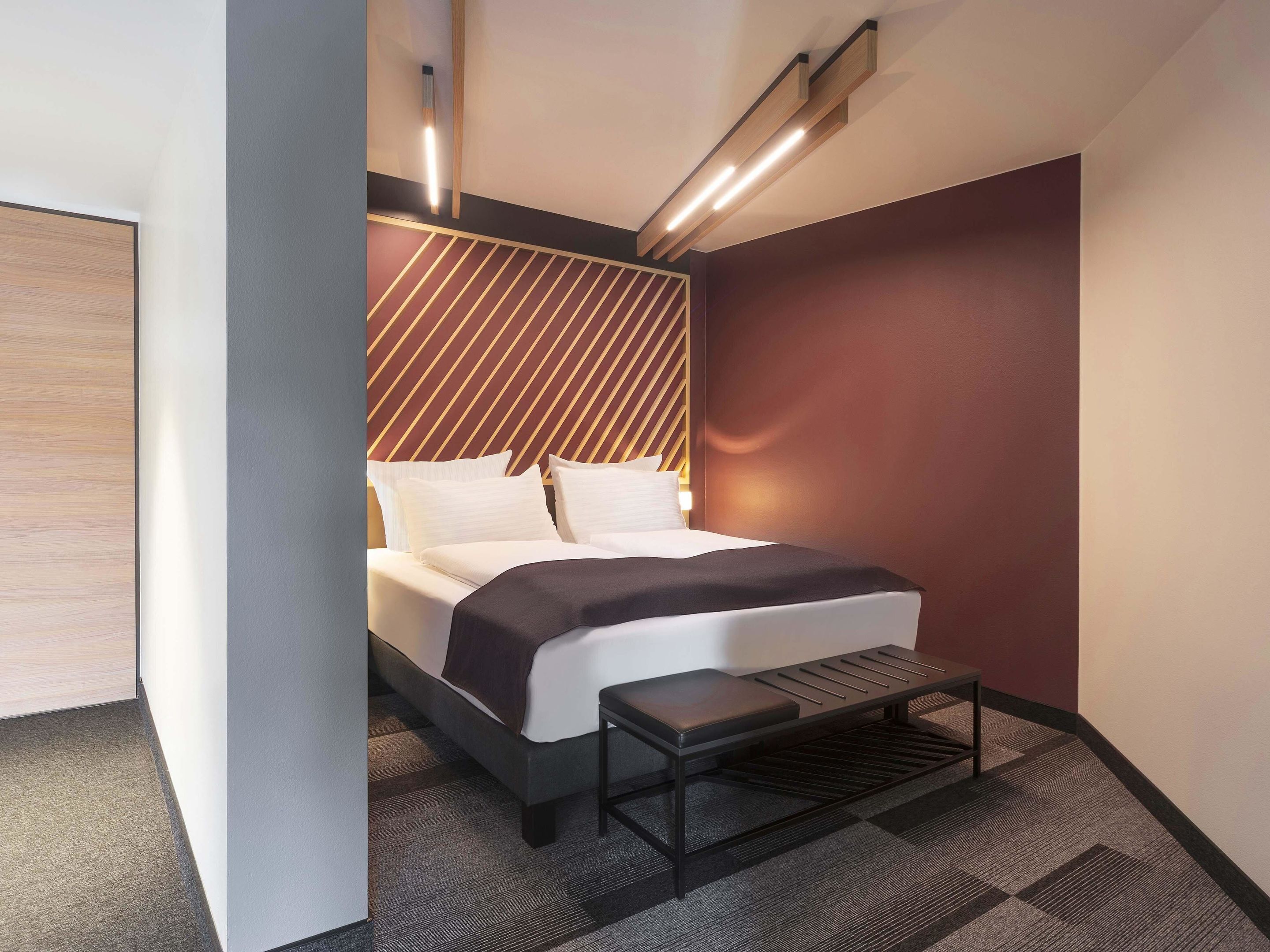 A modern hotel room with a bed, bedside table, and a unique geometric headboard.