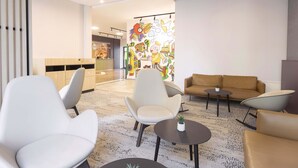 Een moderne lobby met een receptiebalie, een zithoek en een kleurrijke muurschildering.