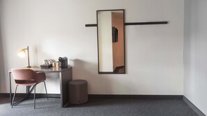 A modern hotel room with a desk, chair, lamp, and a large mirror on the wall.