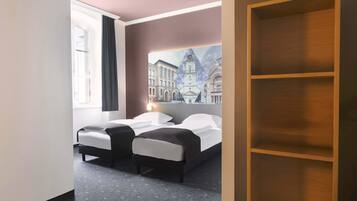 A hotel room with a bed, a nightstand, a window with curtains, and a wall-mounted shelf.