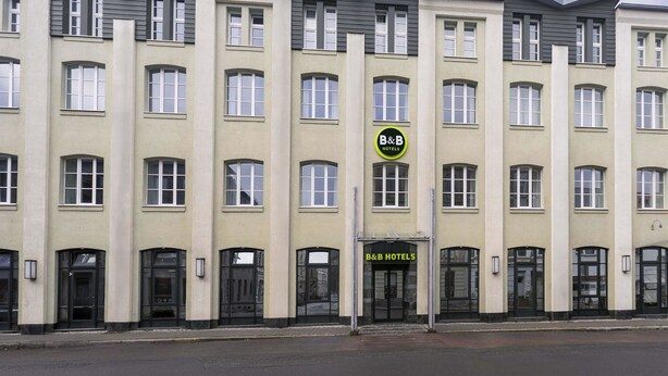Een meerlaags hotelgebouw met een symmetrische gevel, met een centrale ingang met een bord voor B&B Hotels.